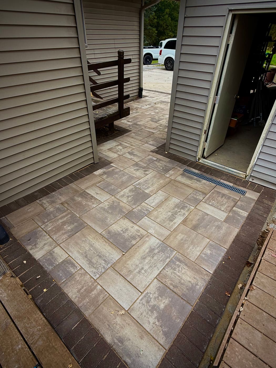 Paver patio with brown border and integrated trench drain between two walls of a Mid-Michigan home